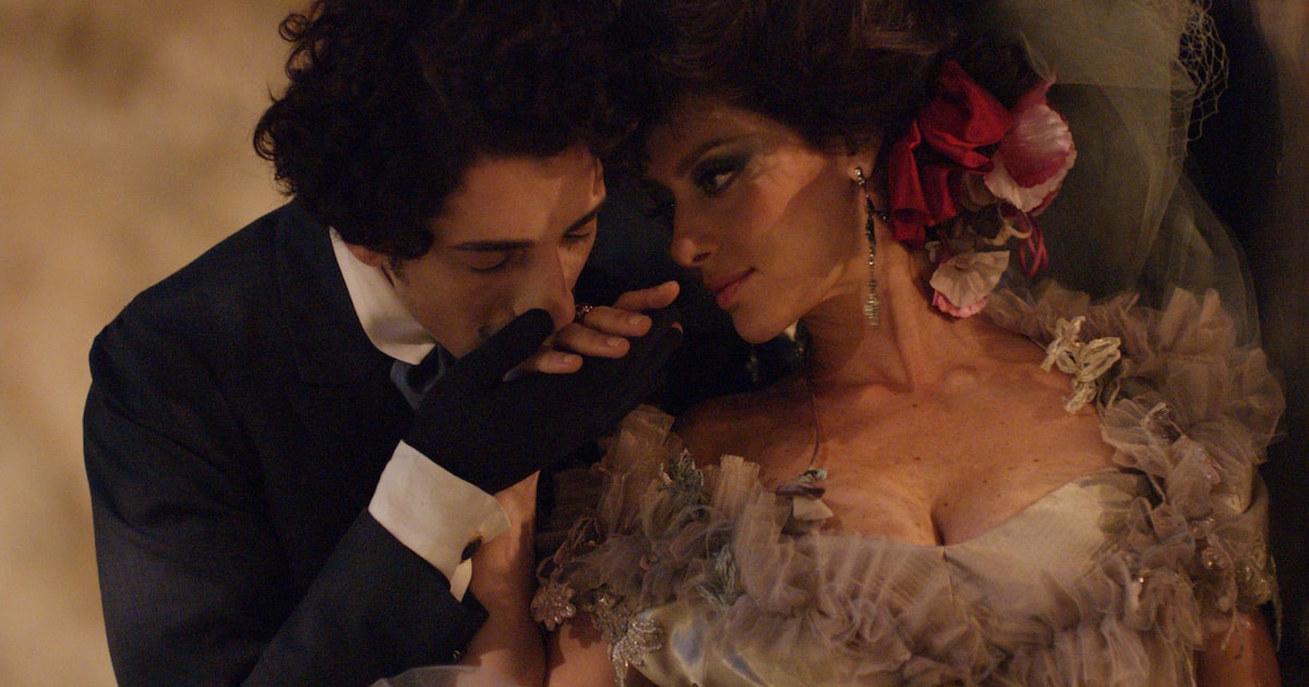 Jornalista segura exemplar de livros de Machado de Assis em frente a uma imagem do autor.