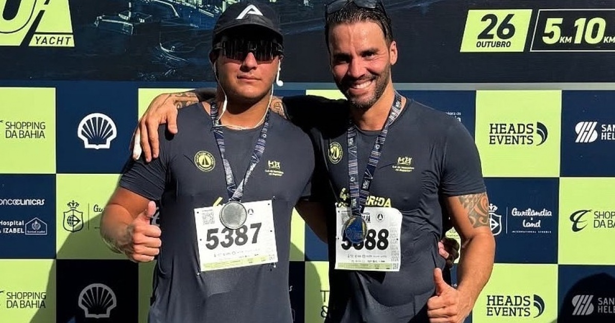 Homem sorridente conversa com filho de esporte em campo de futebol.
