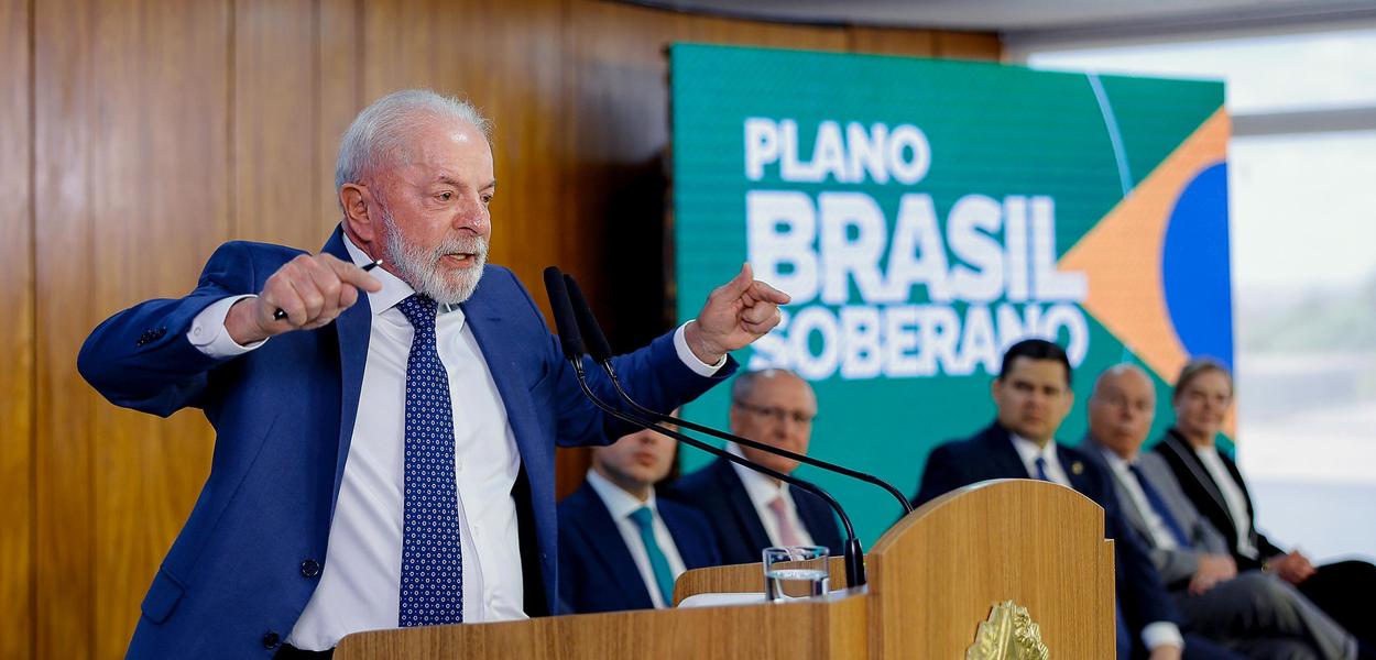 O presidente Lula em reunião de trabalho com ministros, cercado por cartões de visita e documentos governamentais.