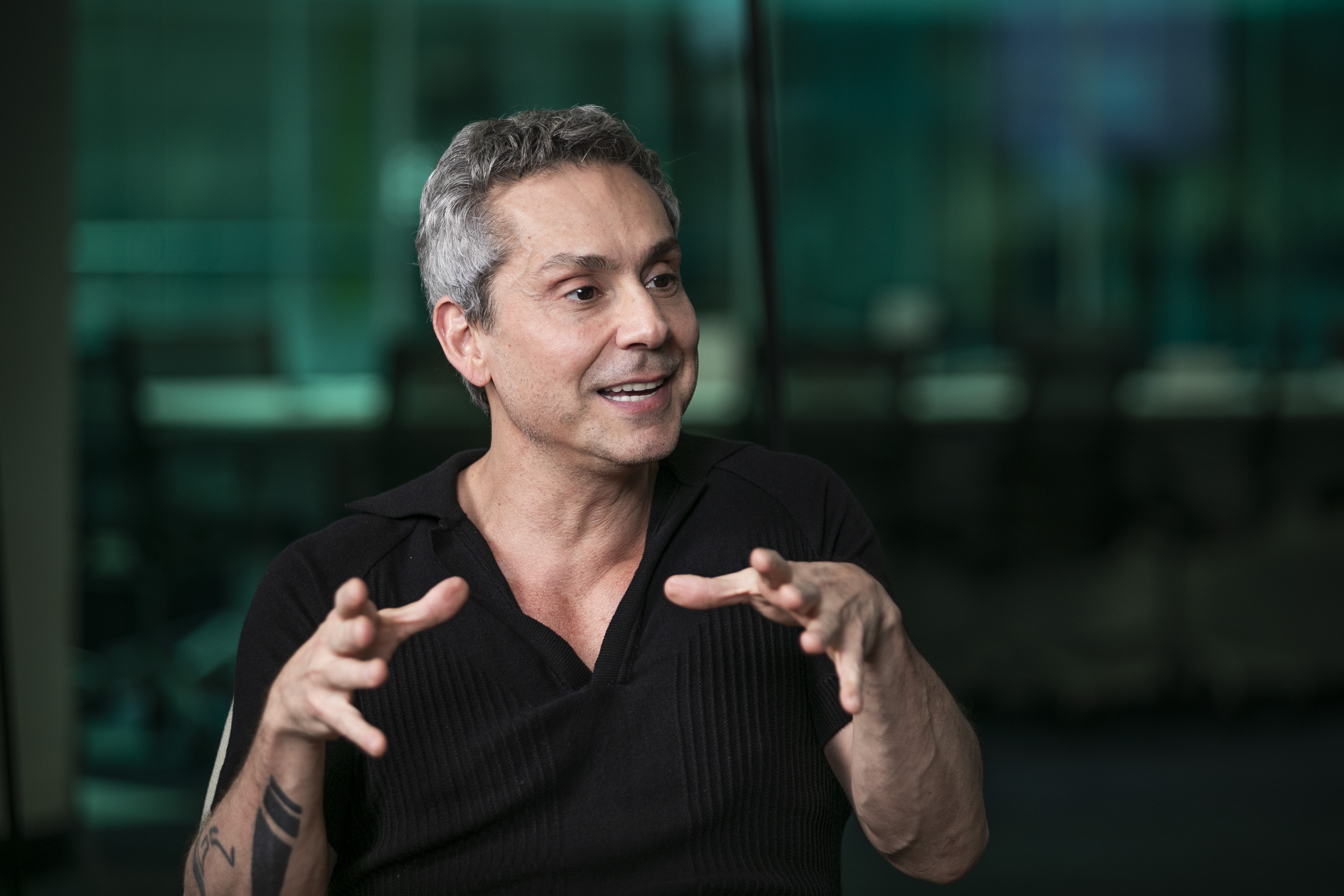 Ator Alexandre Nero posa sorrindo em frente a uma câmera de jornal.