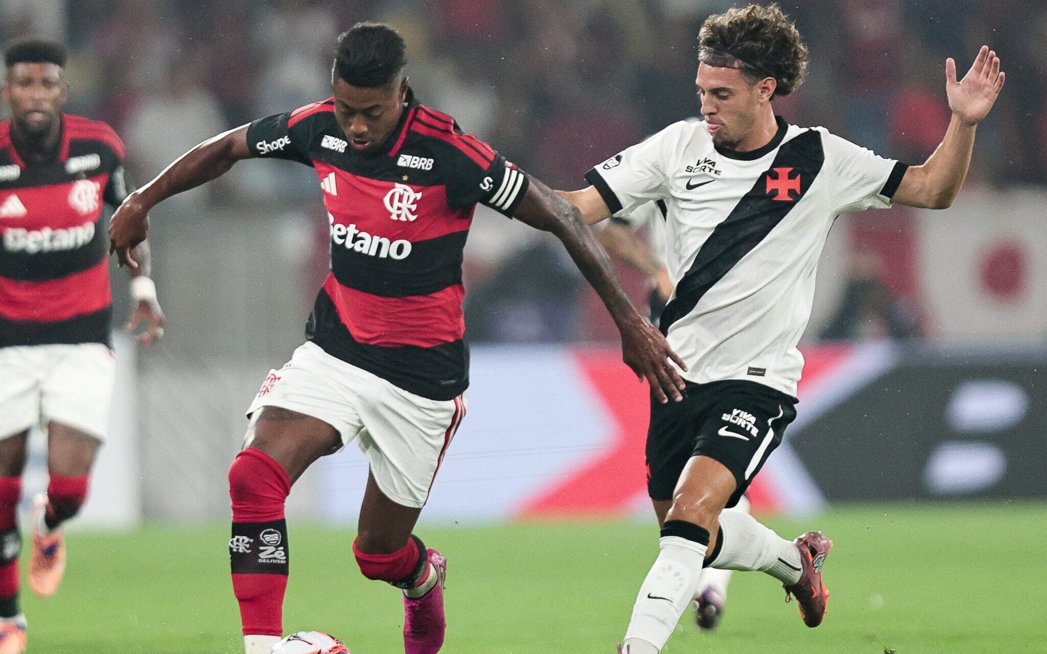 Time do Flamengo em ação no campo de futebol, jogadores em movimento, torcida ao fundo.