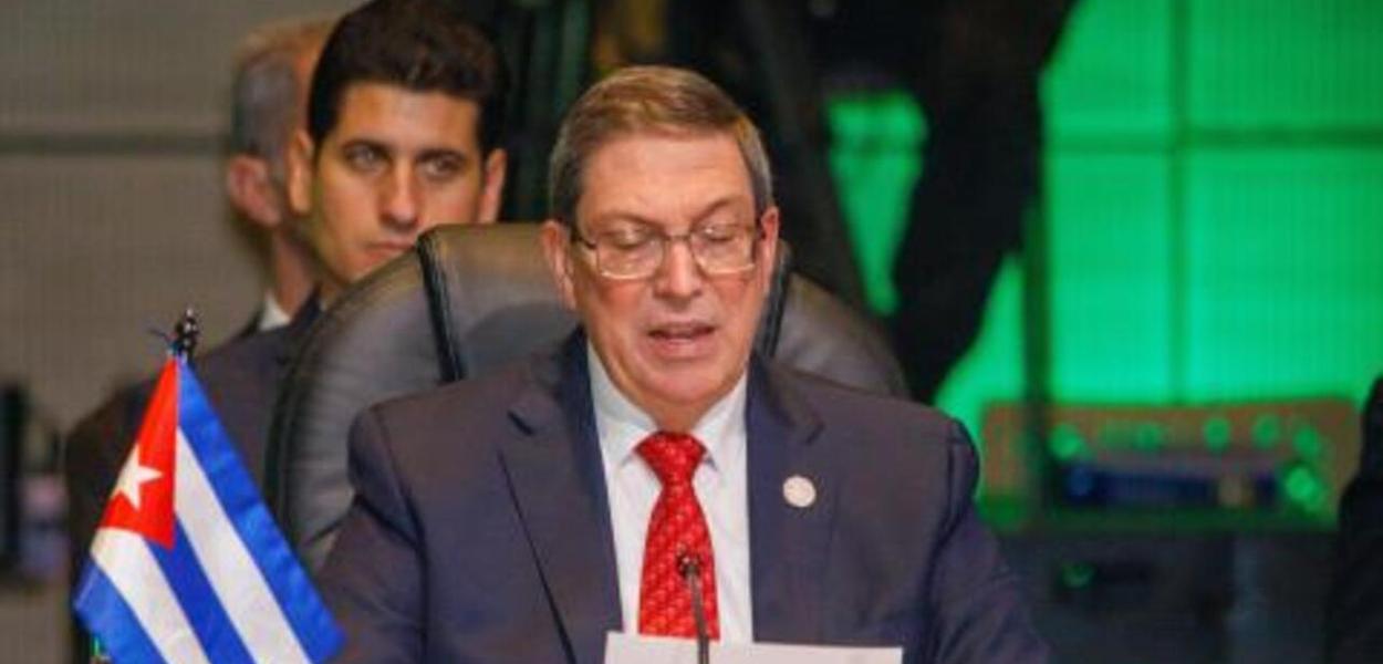Imagem de um jornalista segurando um documento, com um fundo de uma sala de imprensa, enquanto Cuba nega ajuda humanitária dos EUA.