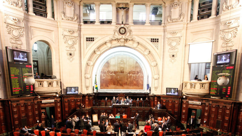 Deputados se manifestam em frente a um prédio da Alerj, com cartazes e bandeiras, em protesto contra associação à milícia.
