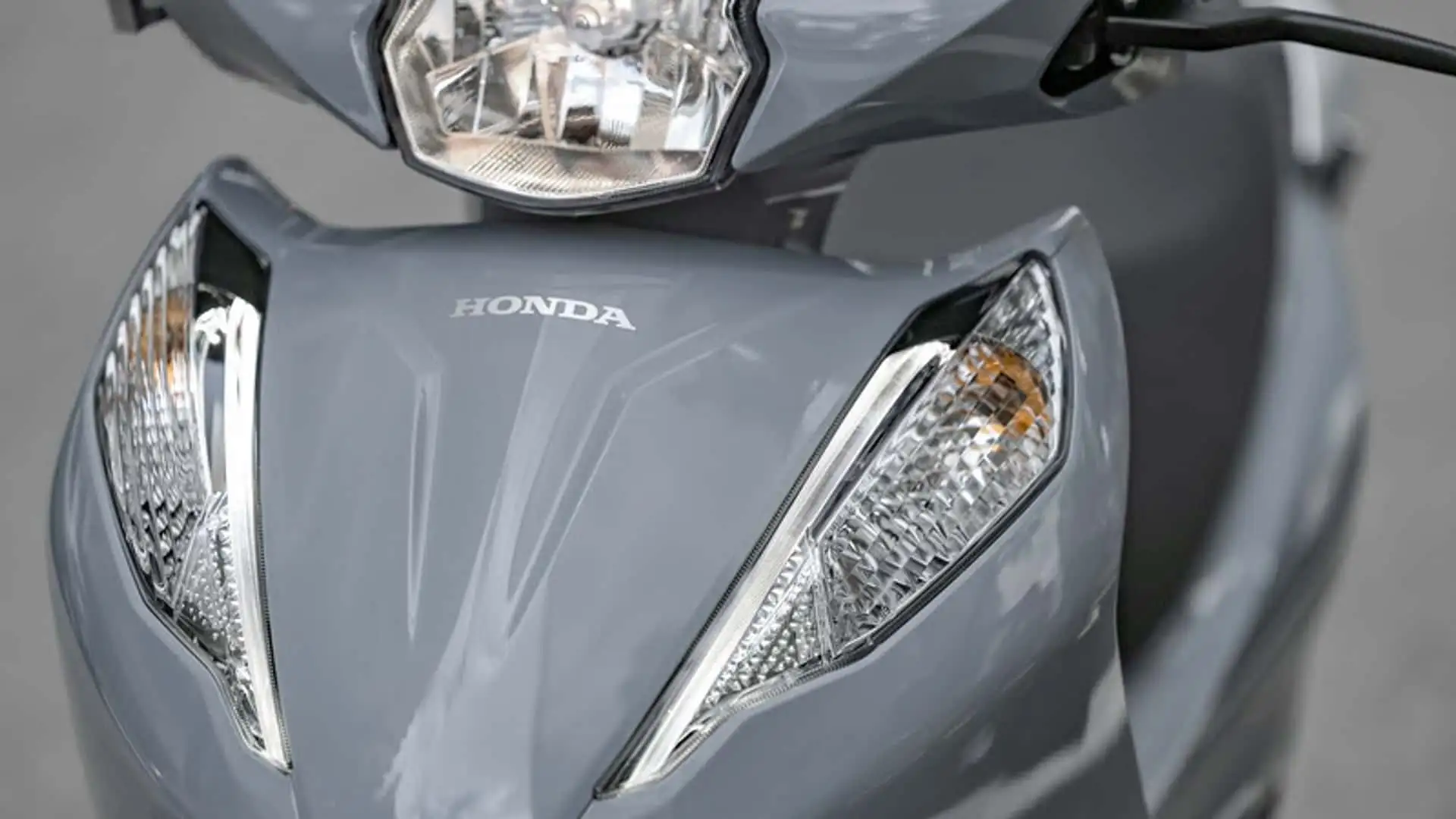 Motorista sentado em uma Honda Biz 2027, com pneus sem câmara e novas cores, em uma estrada urbana.