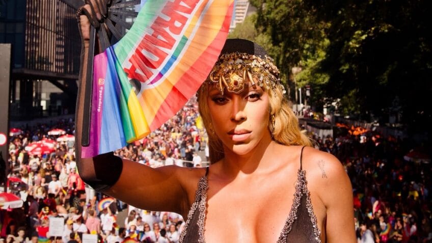 Mulher travesti preta é destaque em parada LGBT+, comemorando vitória política.