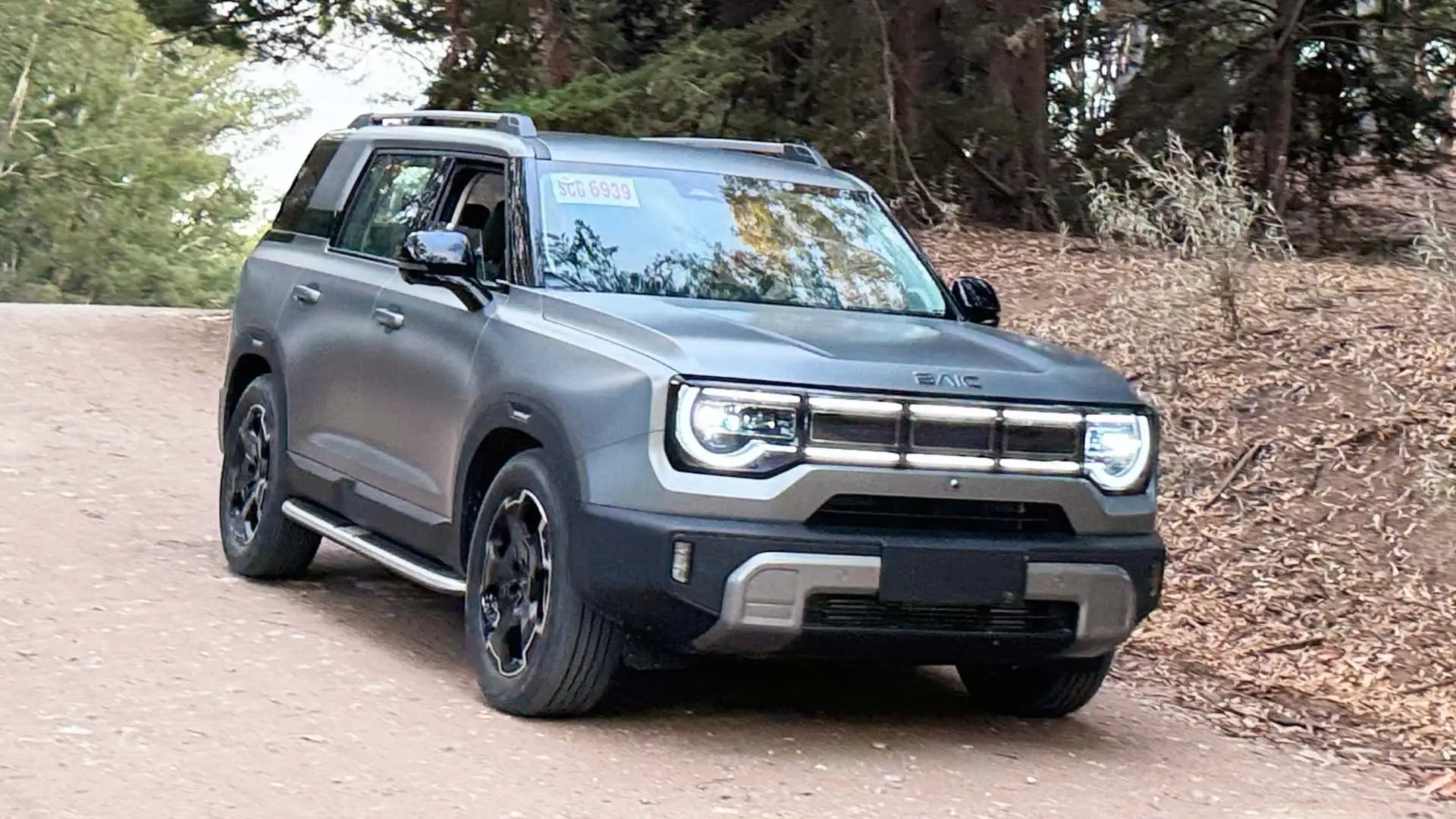 Um jornalista segurando um modelo do BAIC BJ30, com um fundo de uma cidade brasileira.