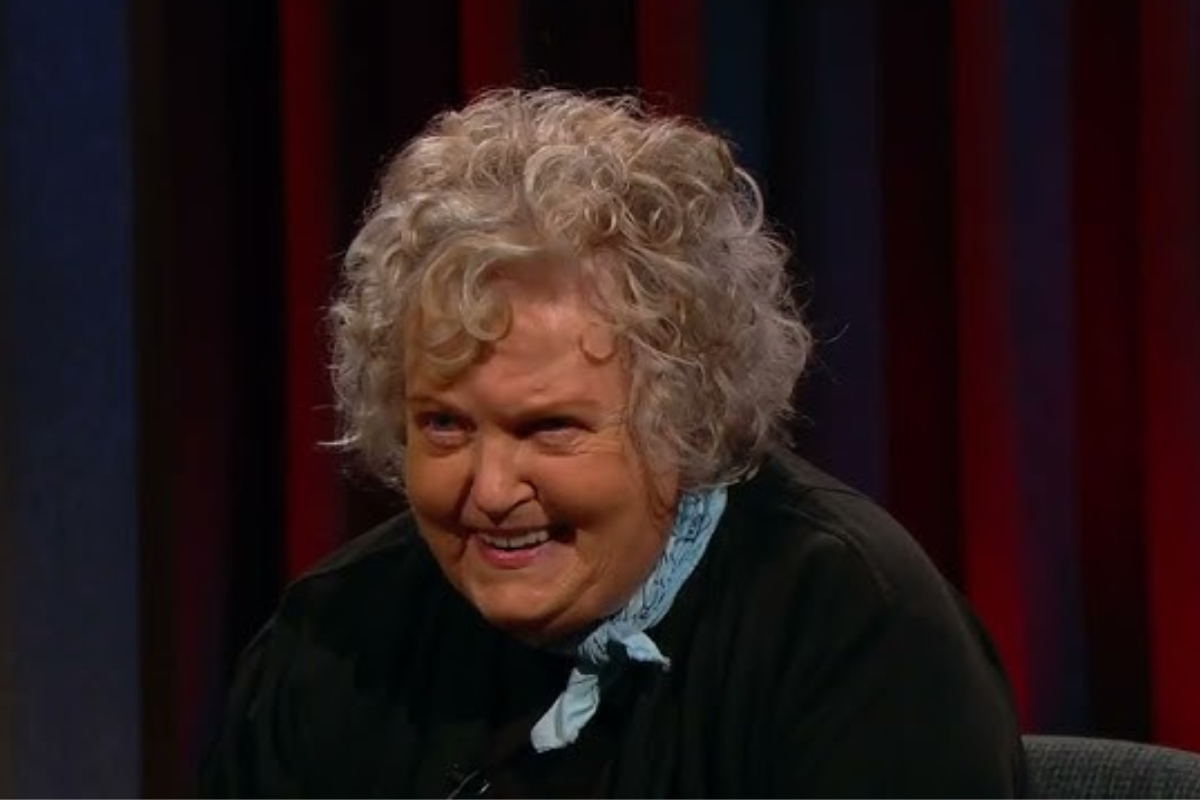 Atriz Brenda Fricker, vencedora do Oscar, sentada em uma cadeira, com uma expressão triste, cercada por jornalistas.