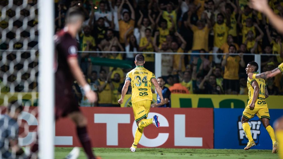 Jornalista sentado à mesa de trabalho, com uma imagem do time LDU e Mirassol em segundo plano.