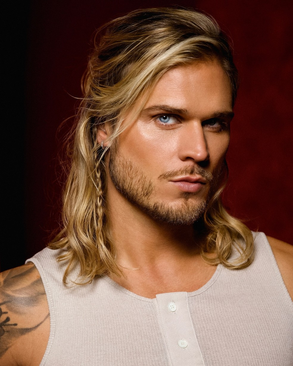 Jogador de futebol famoso sentado em estúdio de arte, com lápis na mão e olhar pensativo.