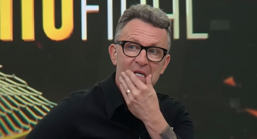 Craque Neto sentado em tribunal, com expressão séria, ao lado de advogados e juiz.