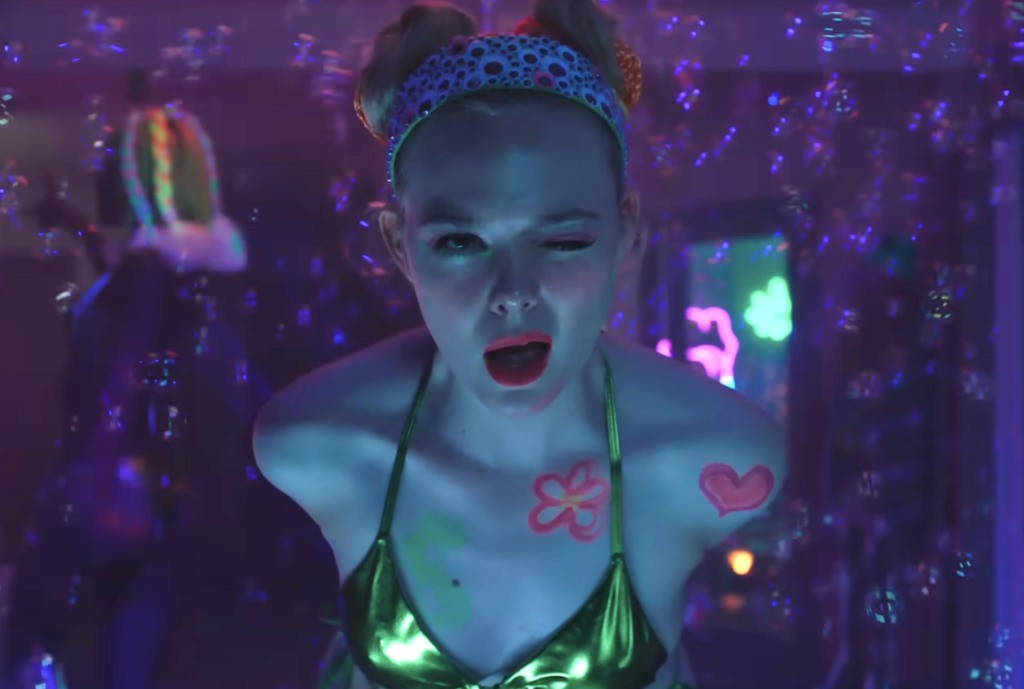 Mulher sentada em uma cadeira, com uma expressão preocupada, cercada por papéis e computadores.