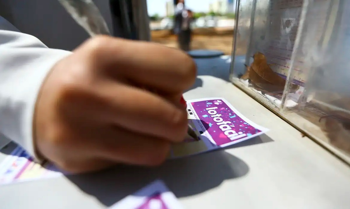 Jornalista segurando um bilhete de Lotofácil com o número acumulado 3662 e um prêmio de R$ 5 milhões.