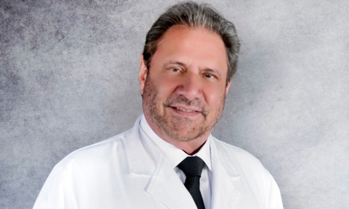 Mulheres sorridentes e saudáveis em torno de uma mesa, com uma equipe de profissionais de saúde em segundo plano.