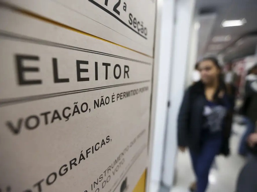 Políticos se reúnem em torno de uma mesa de reunião, com mapas eleitorais e documentos em cima.