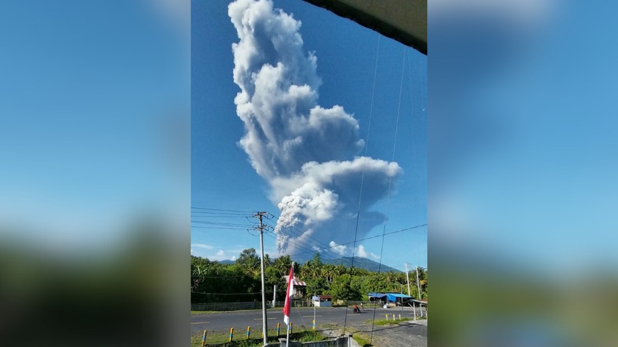 Erupção de vulcão em Indonésia, com nuvens de fumaça e lava cobrindo a paisagem.