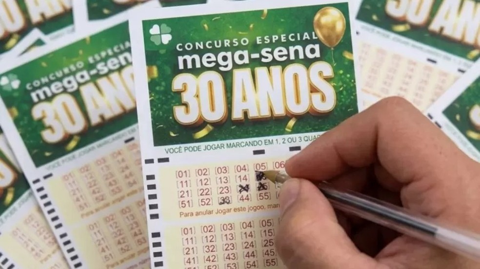 Homem segurando um bilhete de loteria ao lado de um imóvel.