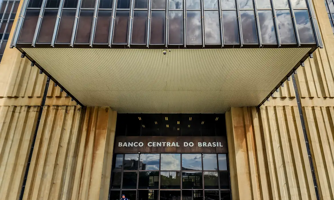 Mercado financeiro em reunião, com gráficos de inflação ao fundo.