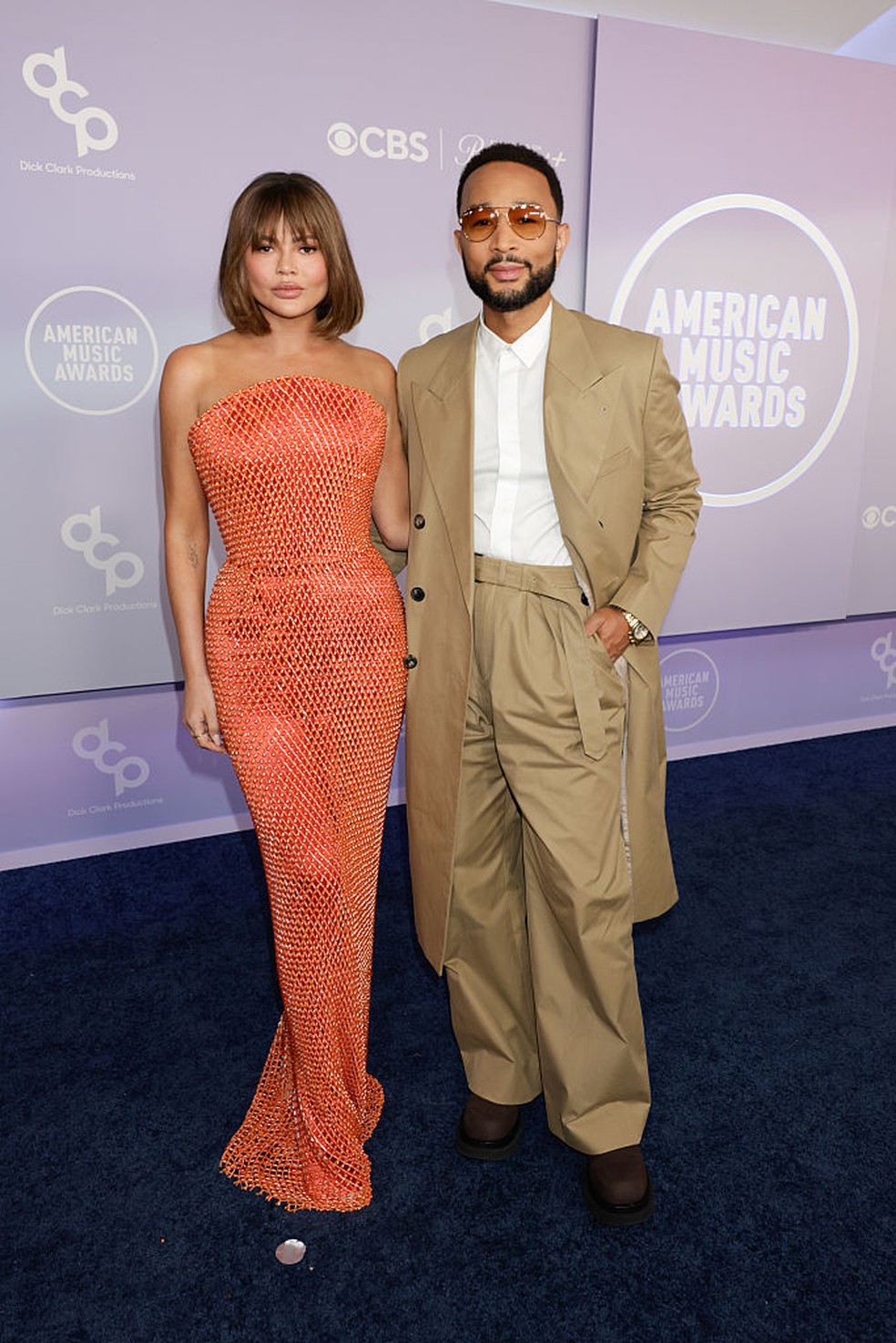 Chrissy Teigen tropeça no tapete vermelho do AMAs 2026, reagindo com humor e elegância.