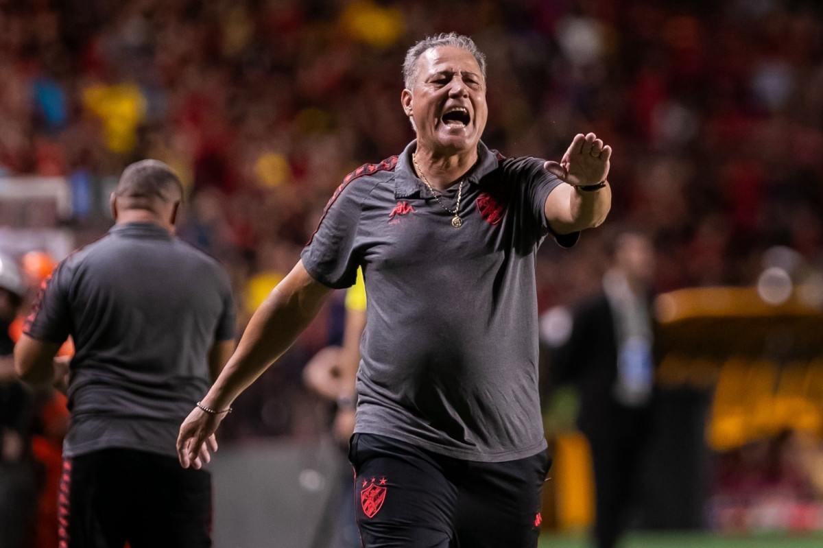 Jornalista segurando uma página de notícia com o título "Sport enfrenta o Náutico na Série B".