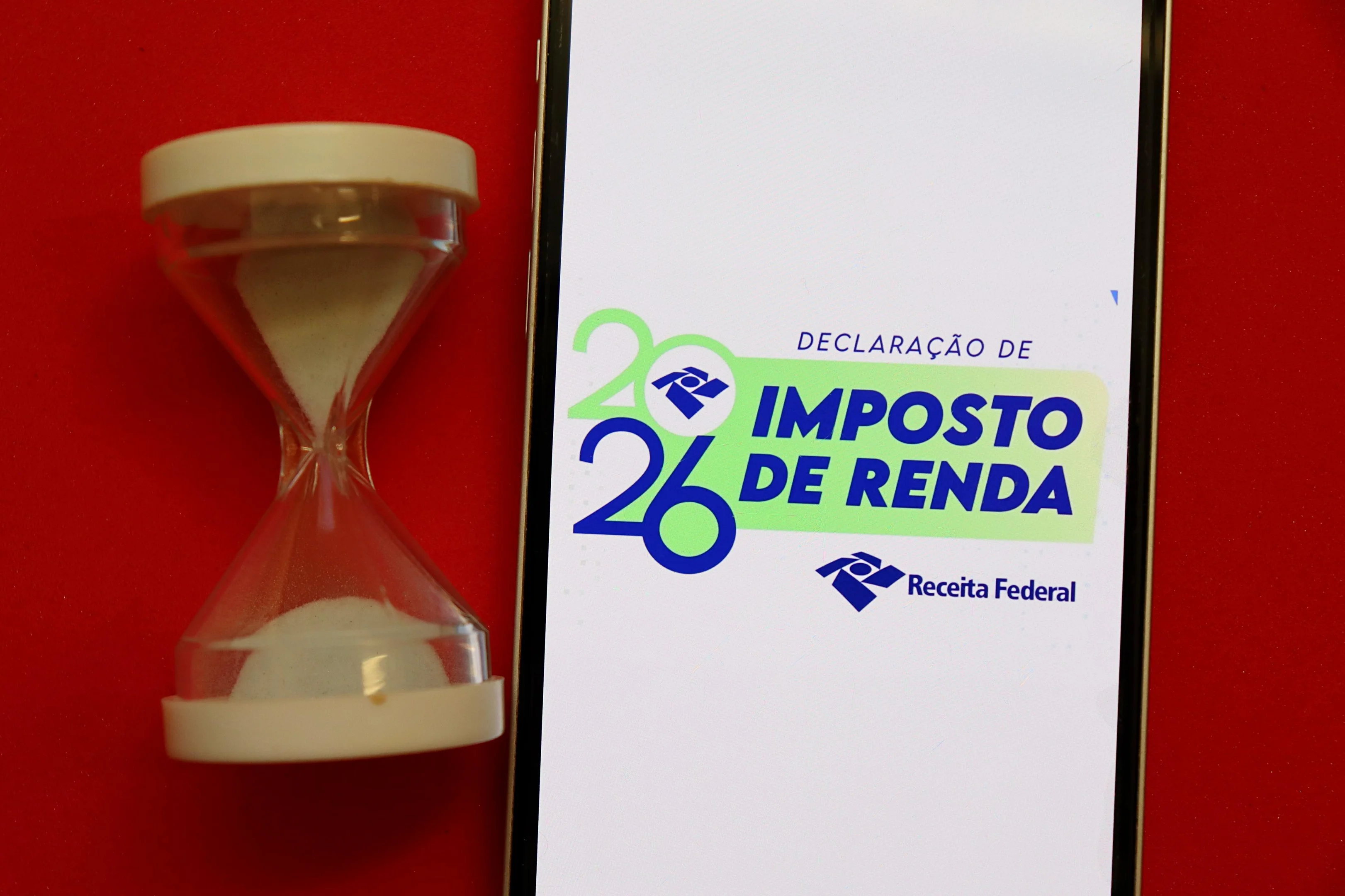 Pessoa segurando calendário e computador, com tela mostrando dados de imposto de renda.
