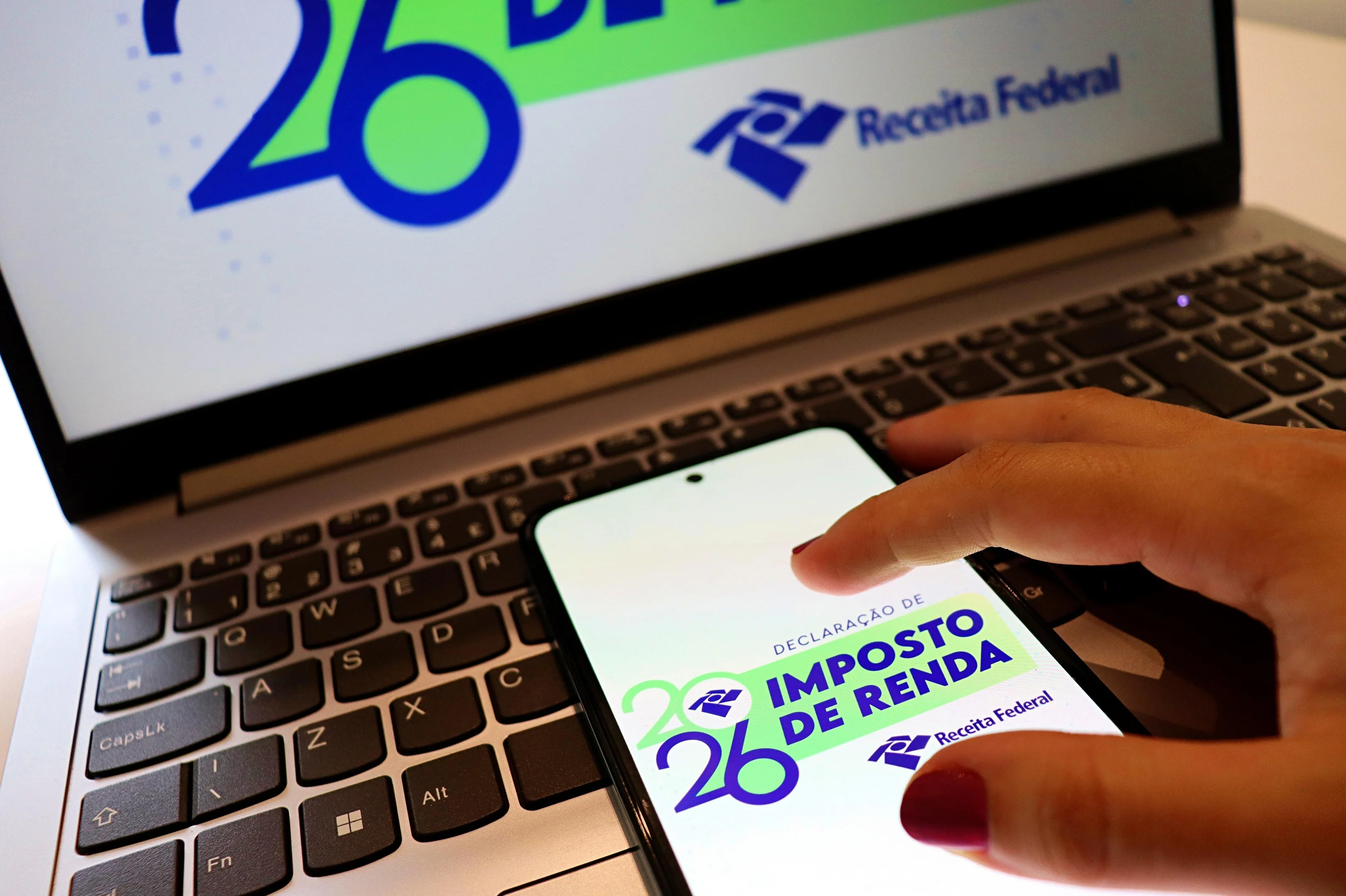 Pessoa segurando calendário e computador, com tela mostrando dados de imposto de renda.