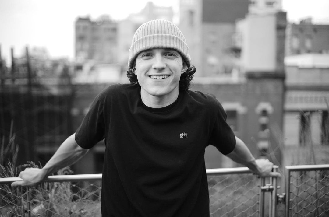 Tom Holland posa em frente a uma tela de cinema com uma expressão pensativa.