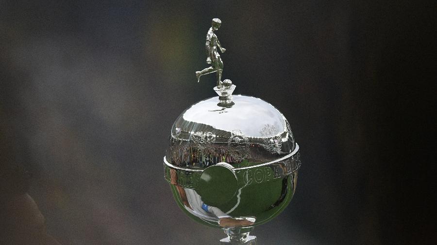 Jornalista em frente a uma tela de TV mostrando a logo da Copa Libertadores.