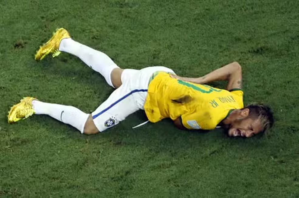Luana Piovani sorri enquanto segura um cartaz com uma mensagem sarcástica sobre a lesão de Neymar.