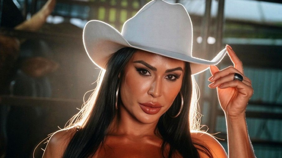 Gracyanne Barbosa sentada em frente a uma mesa, com um olhar desapontado e um frasco vazio de remédio para emagrecer.