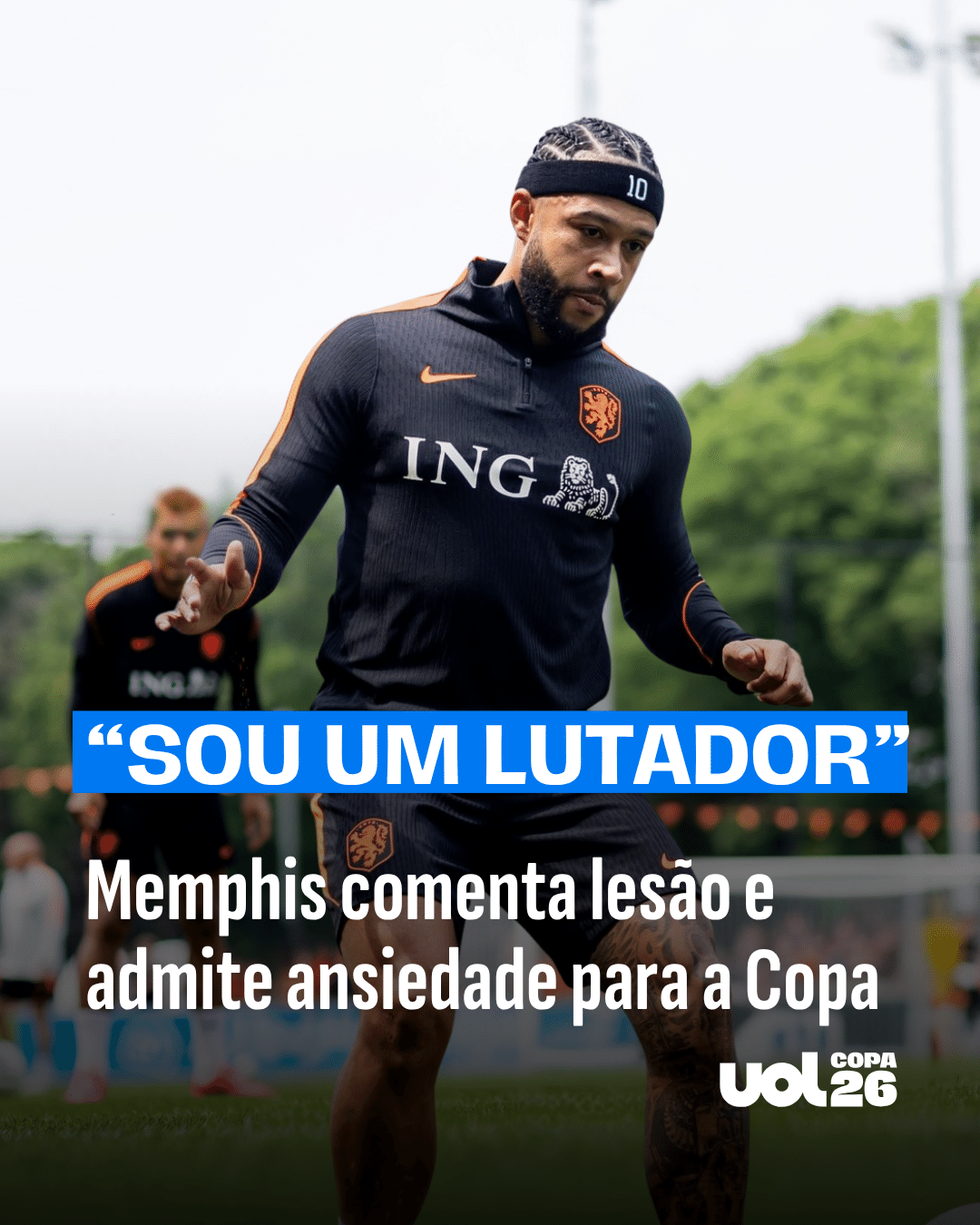 Jornalista sentado à mesa de trabalho, com papel e caneta, olhando para tela de computador com notícias de Copa.