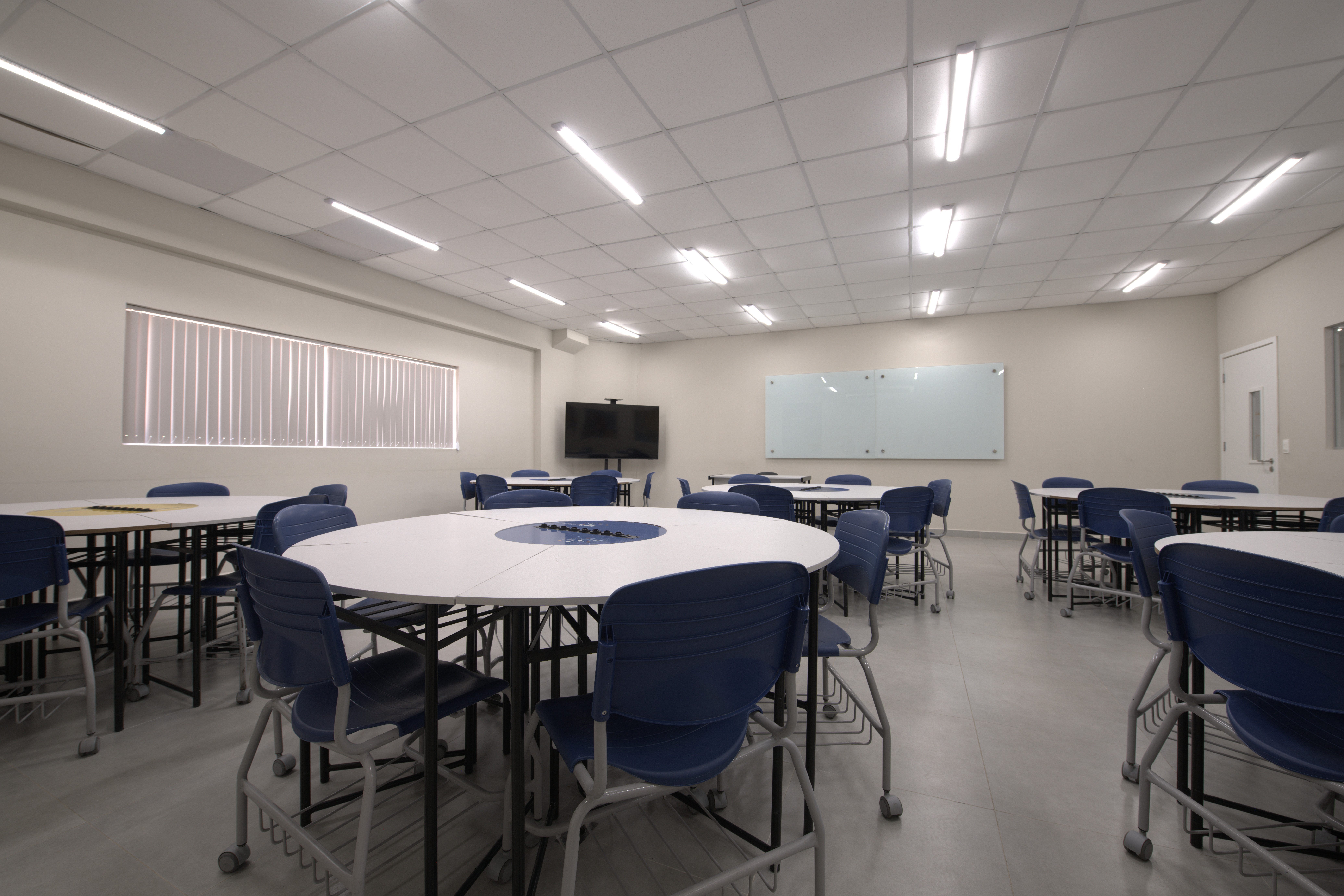 Estudantes em aula, com professores e materiais educacionais em uma sala de aula moderna.