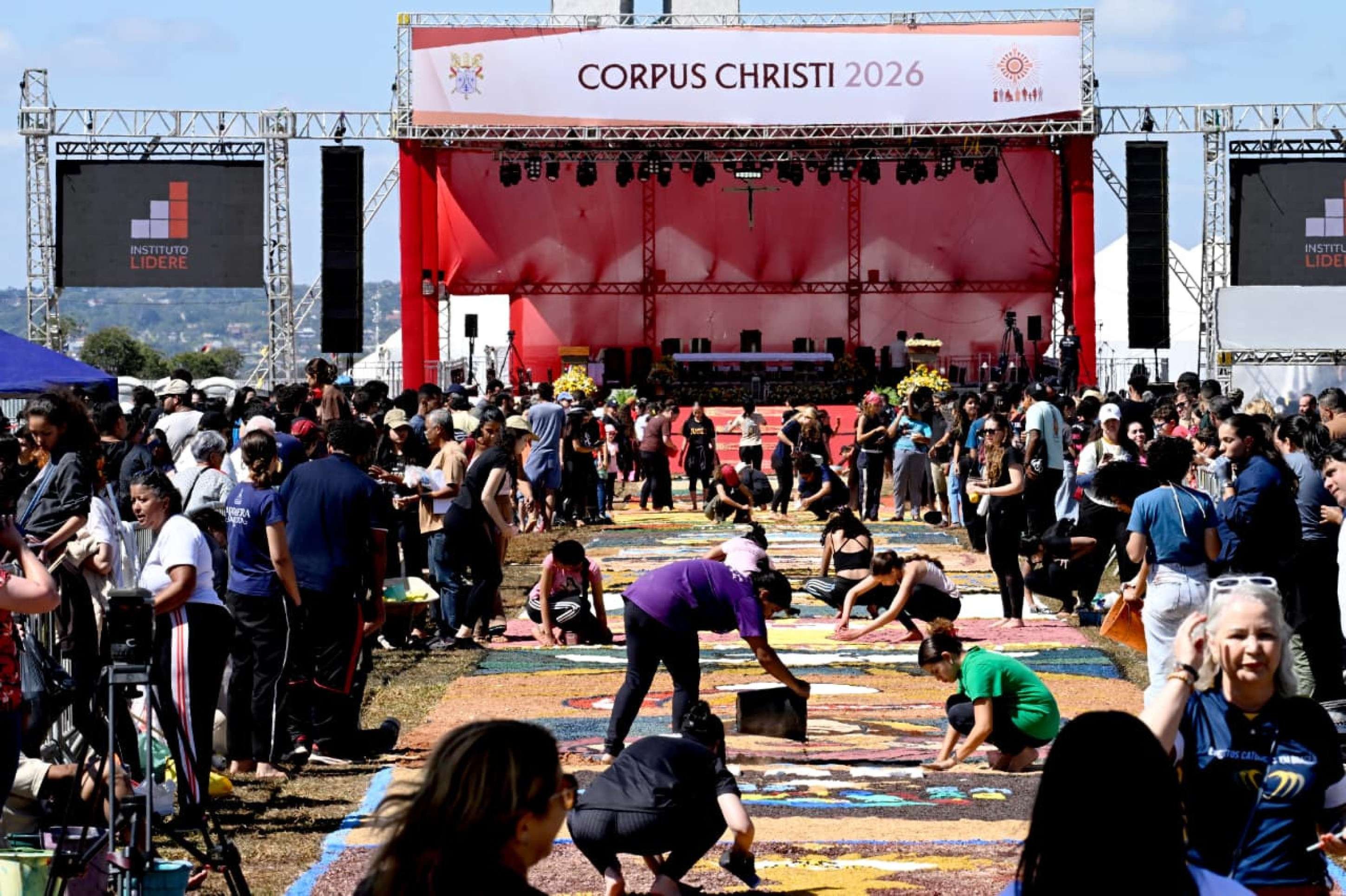 Pessoas reunidas na Esplanada, montando um tapete colorido para a celebração de Corpus Christi.