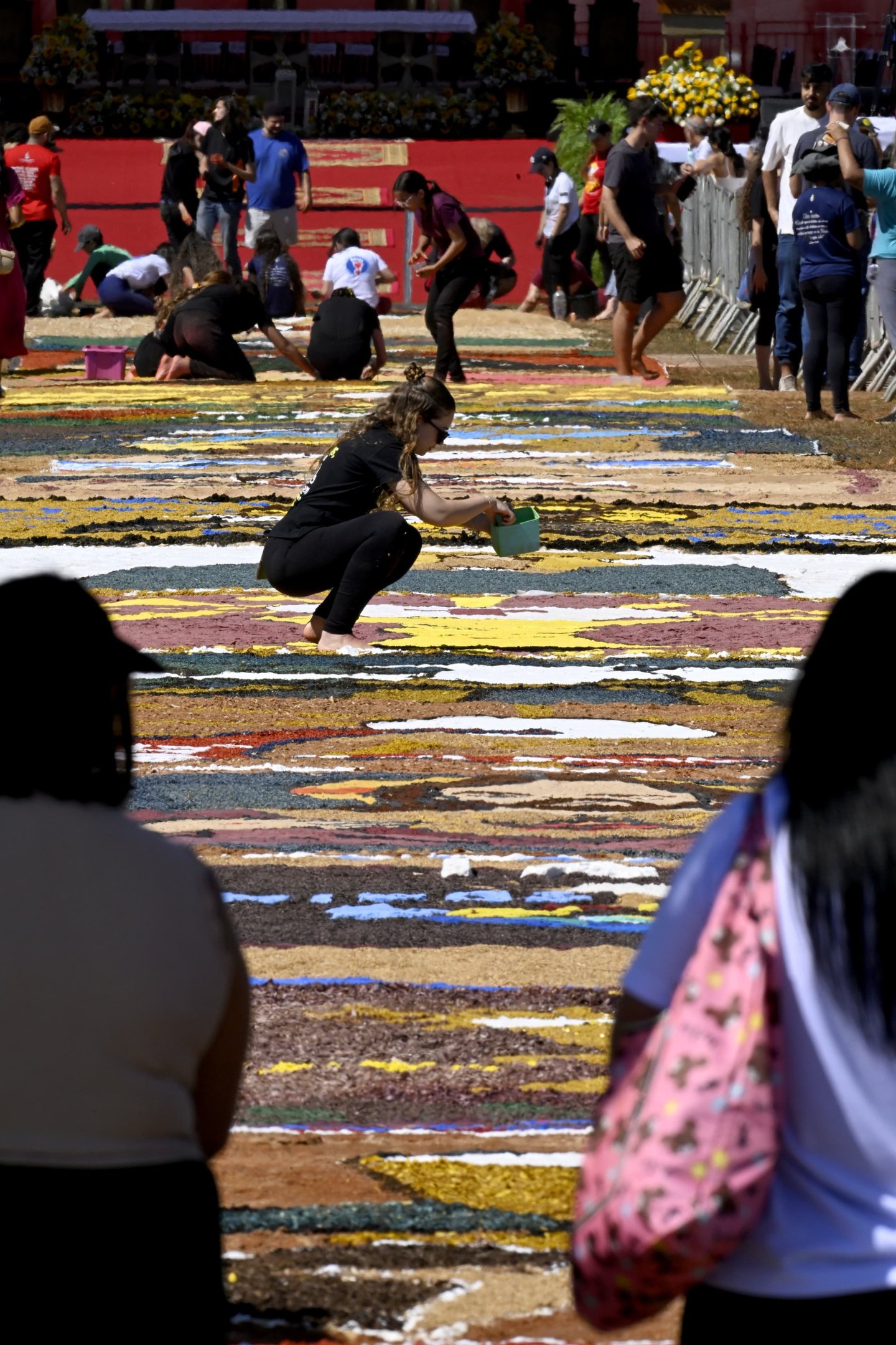 Pessoas reunidas na Esplanada, montando um tapete colorido para a celebração de Corpus Christi.