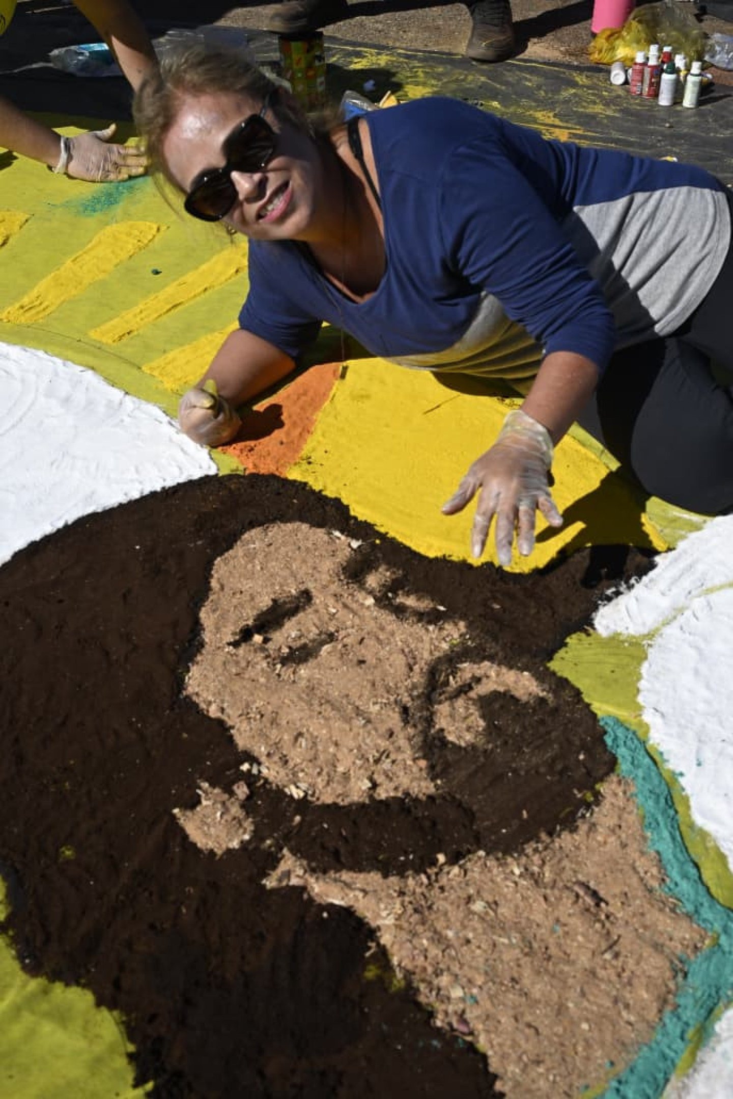 Pessoas reunidas na Esplanada, montando um tapete colorido para a celebração de Corpus Christi.