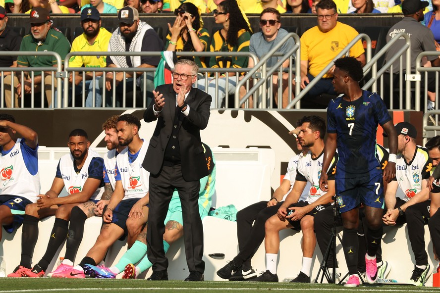 Ancelotti sentado à mesa de imprensa, com Wesley ao seu lado, ambos com expressões sérias.
