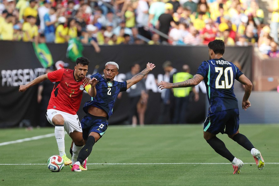 Jogador de futebol sentado em uma cadeira, cercado por médicos e treinadores, com um olhar preocupado.