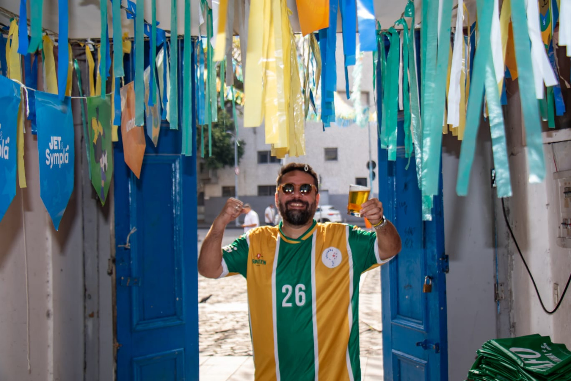 Mulheres dançando samba ao fundo de uma mesa com cartazes de jogos da Copa do Mundo.