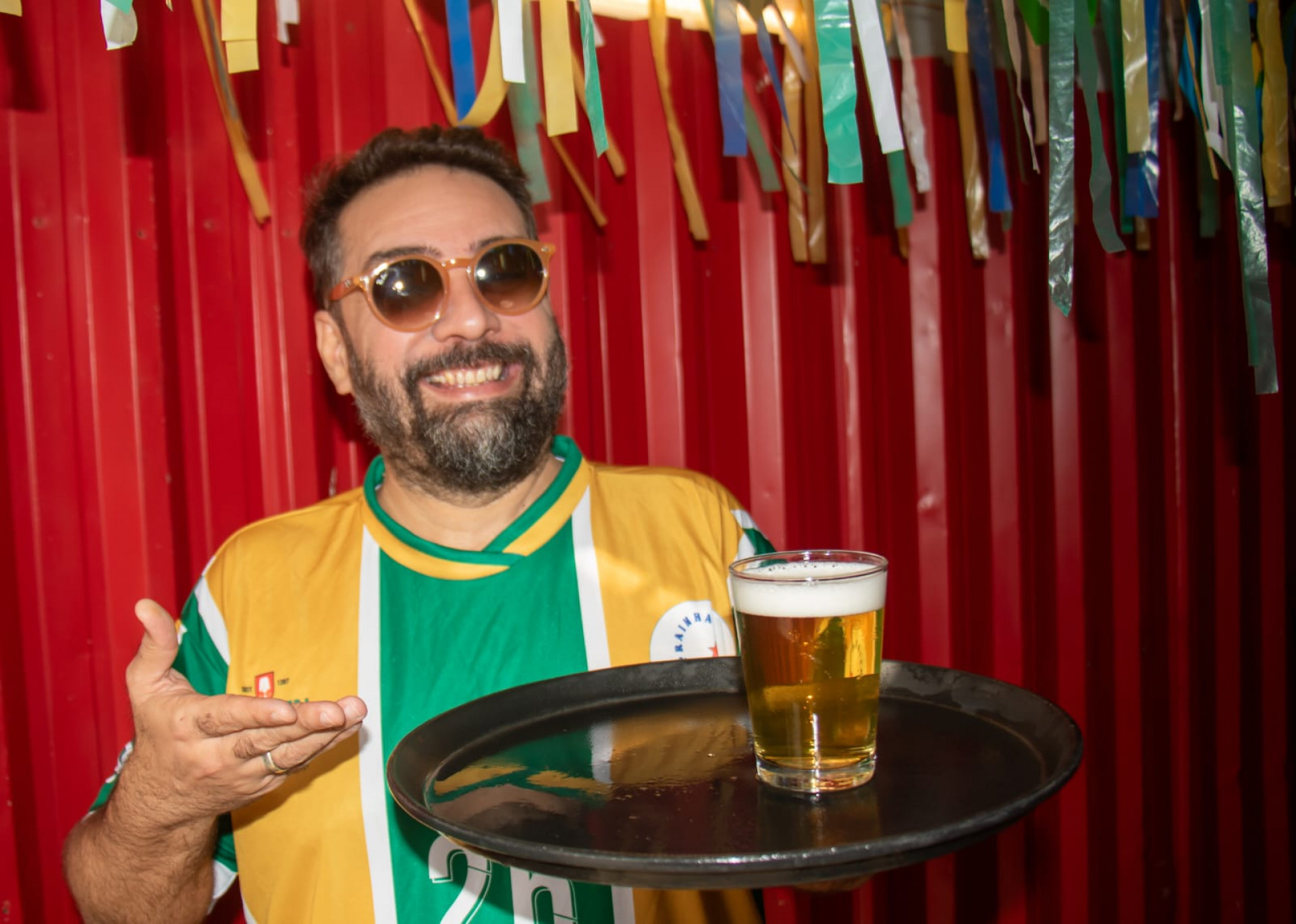Mulheres dançando samba ao fundo de uma mesa com cartazes de jogos da Copa do Mundo.
