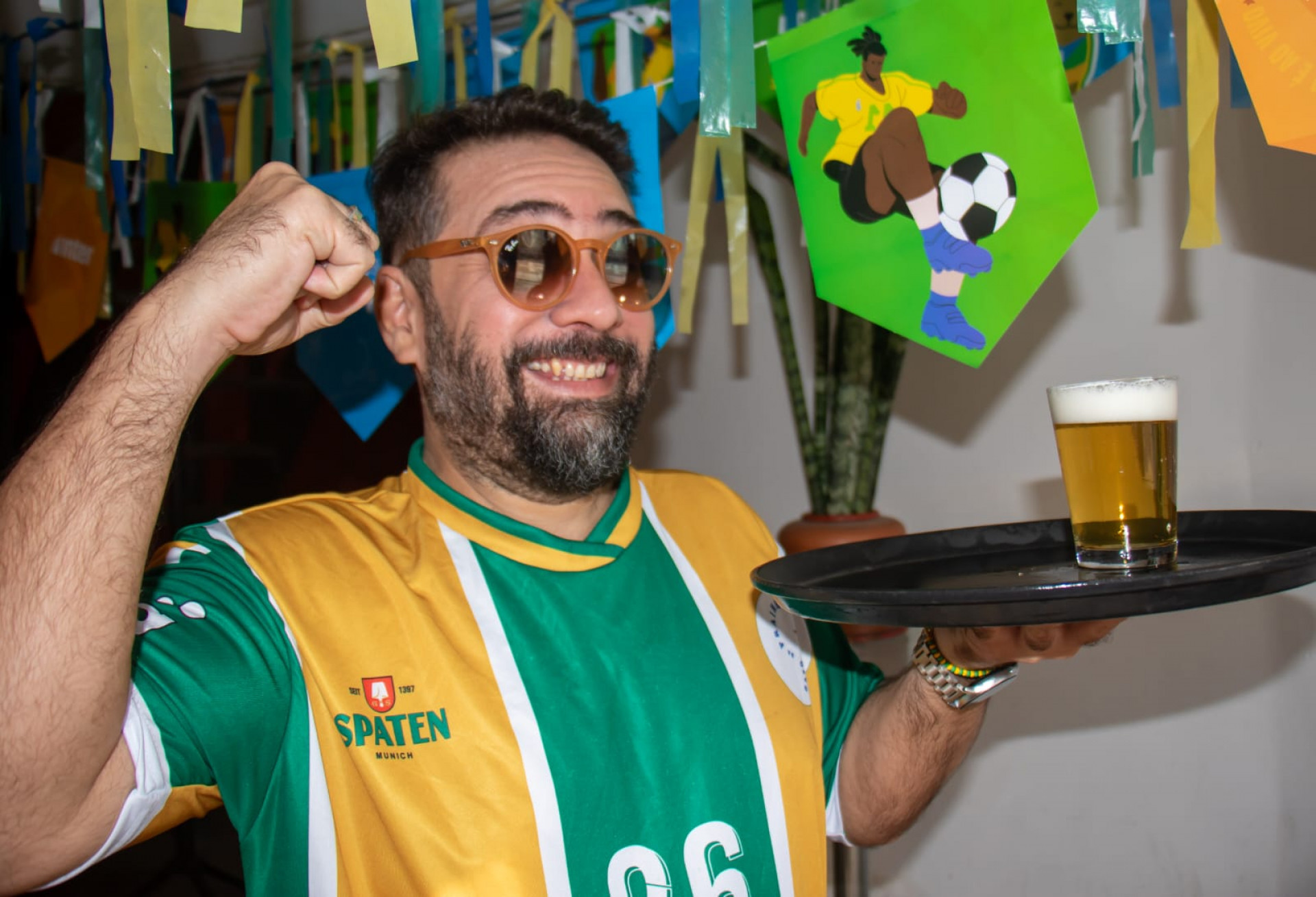 Mulheres dançando samba ao fundo de uma mesa com cartazes de jogos da Copa do Mundo.