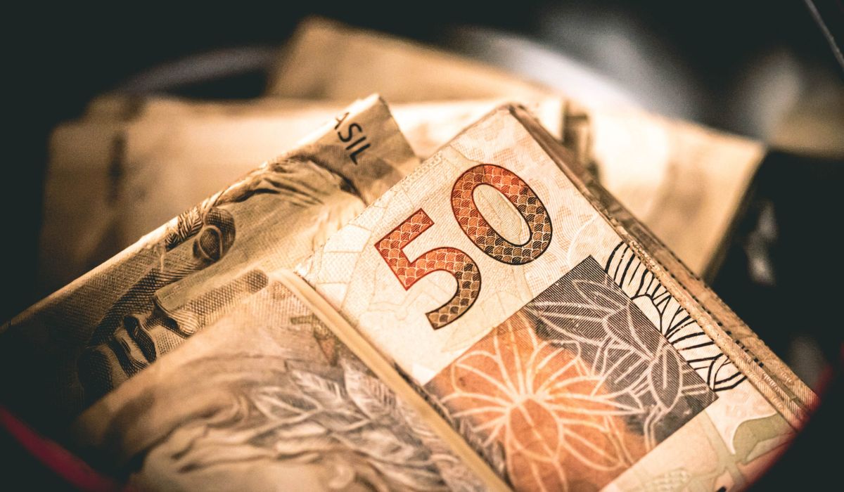 Três pessoas celebram ao lado de uma grande tela exibindo números da Lotofácil.