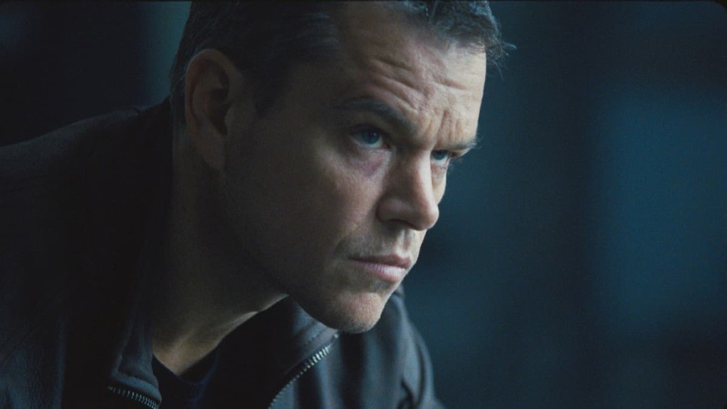 Matt Damon sentado em frente a uma mesa de reunião, com um olhar pensativo, em um cenário de escritório.