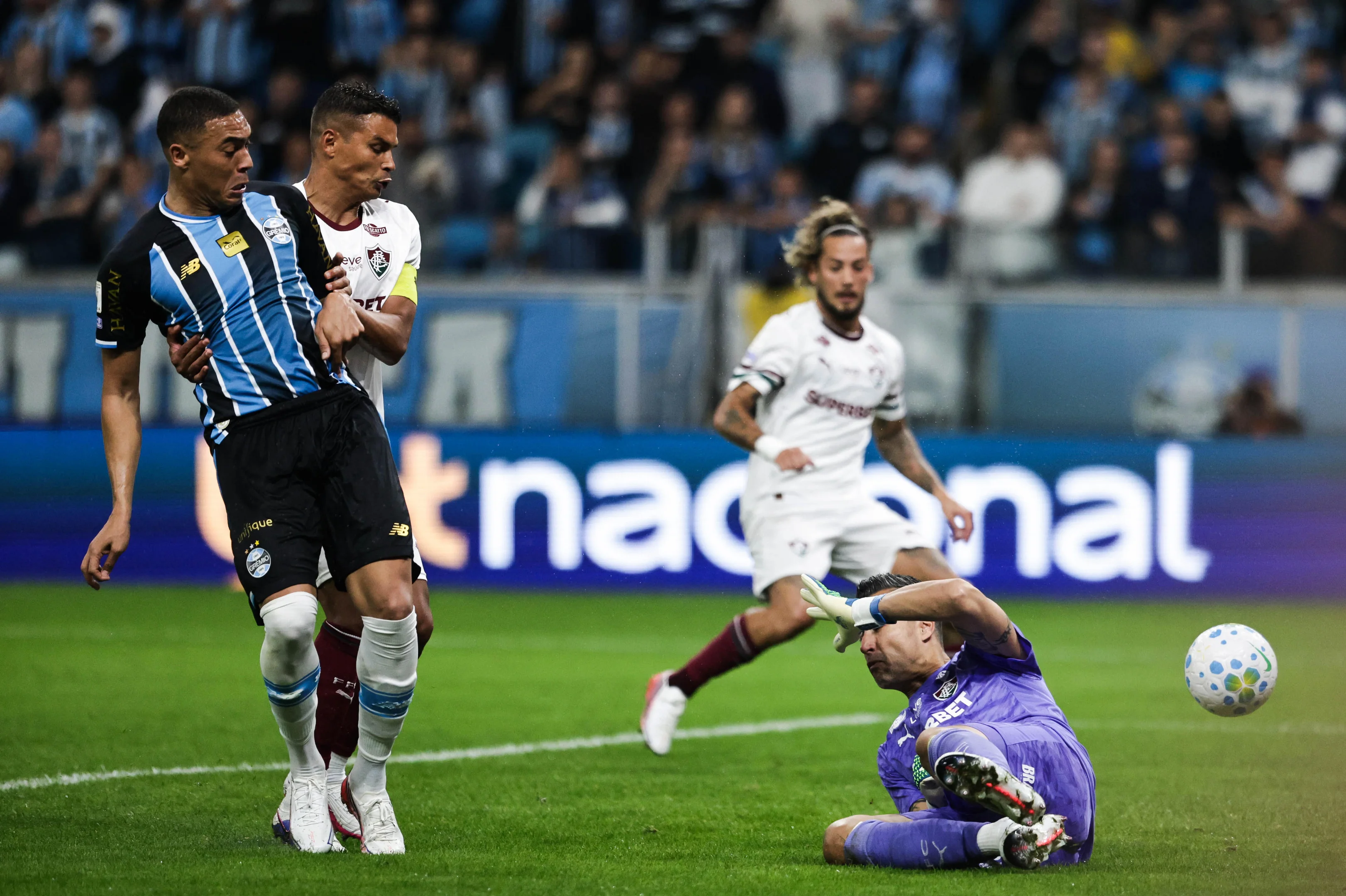 Carlos Vinícius em entrevista, com expressão pensativa, sentado em frente a uma mesa com uma camisa do Grêmio.