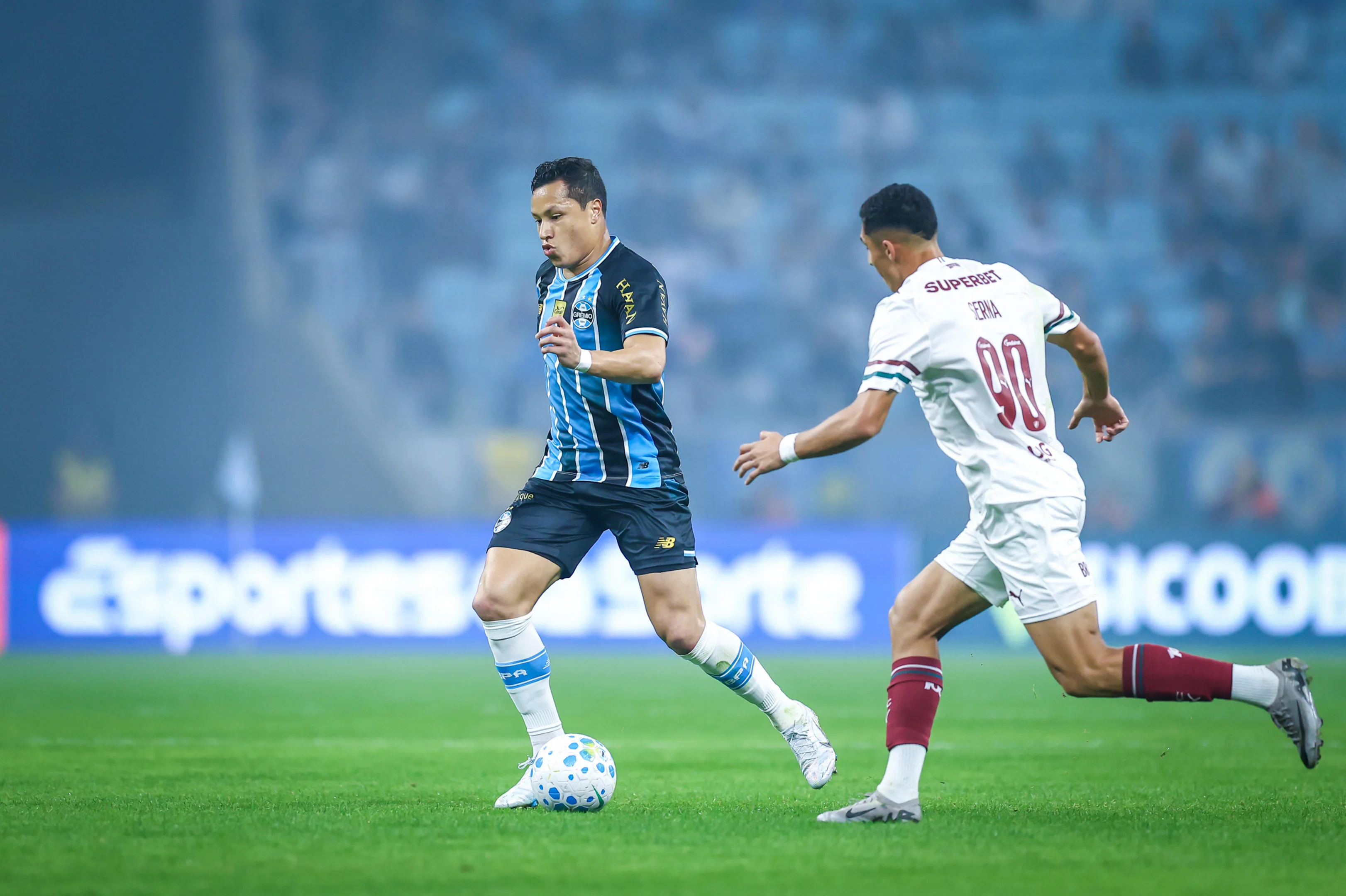 Marlon sorrindo e abraçado por jogadores após anúncio de retorno ao Grêmio após lesão.