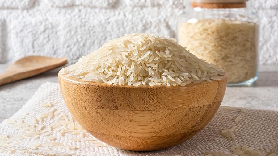 Pessoa lavando arroz em uma pia, com um jornalista observando em segundo plano.