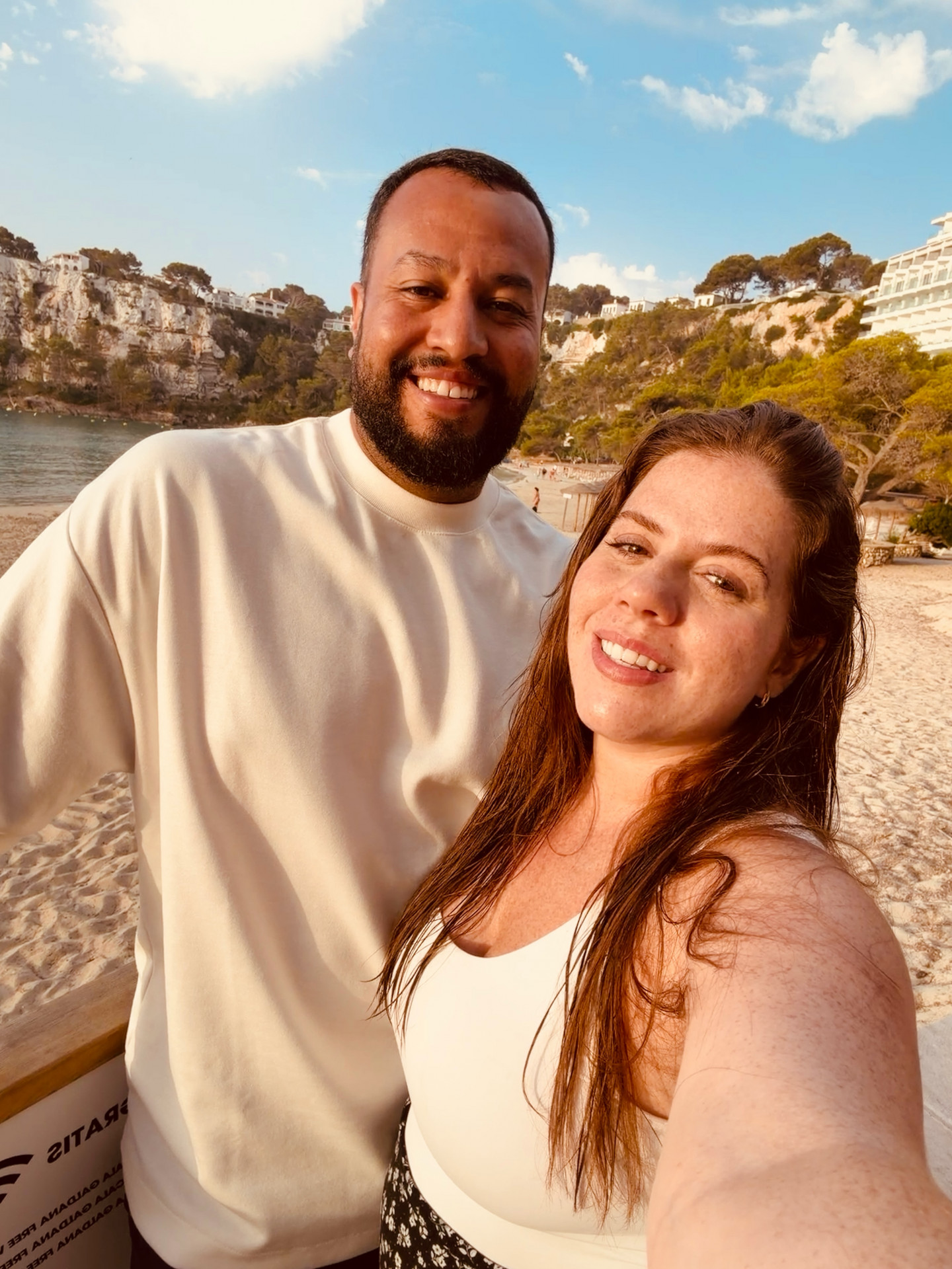 Grávida de oito meses, Tati Machado sorri ao lado de seu marido, segurando um cartão com o nome do bebê.