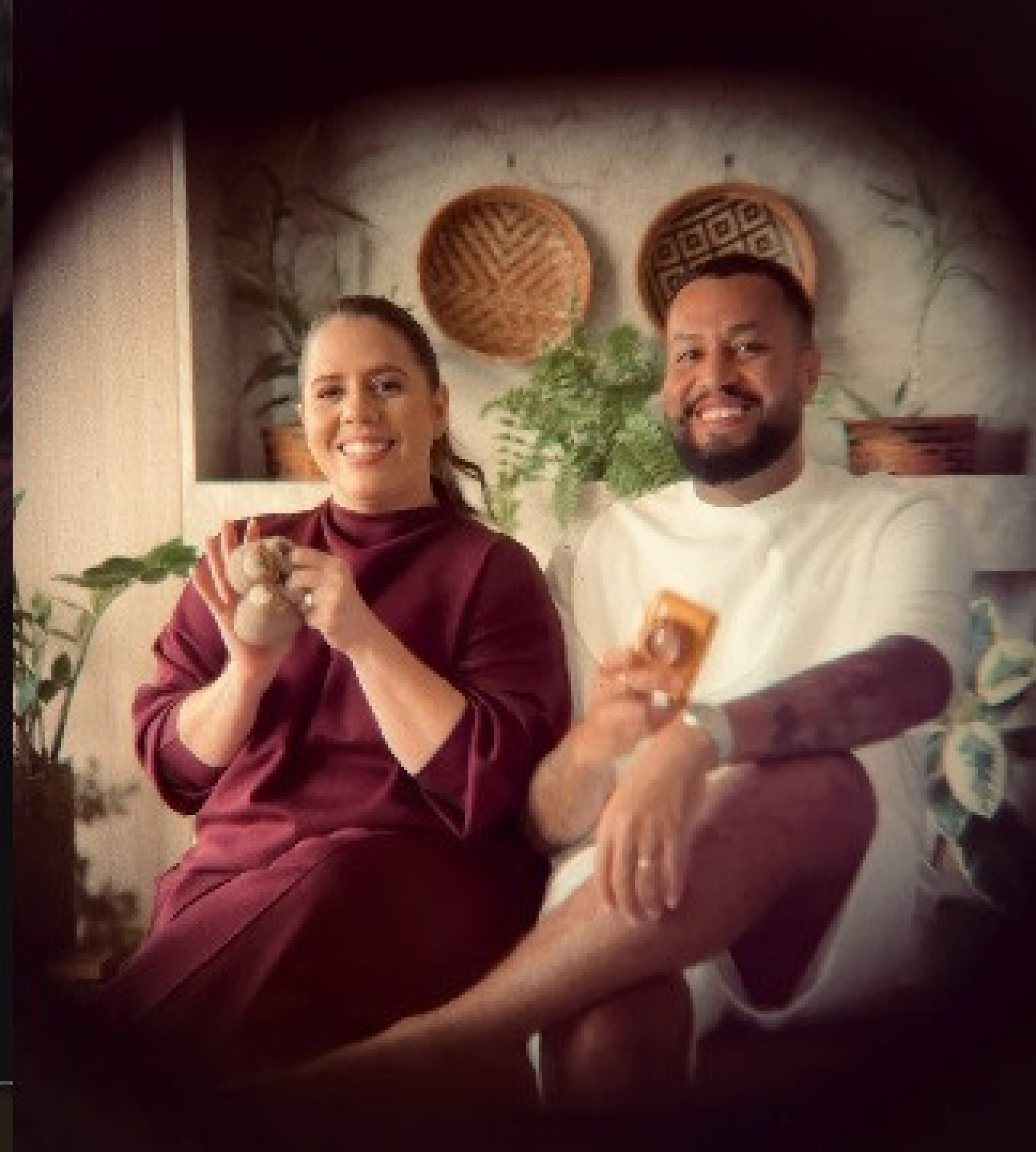 Grávida de oito meses, Tati Machado sorri ao lado de seu marido, segurando um cartão com o nome do bebê.