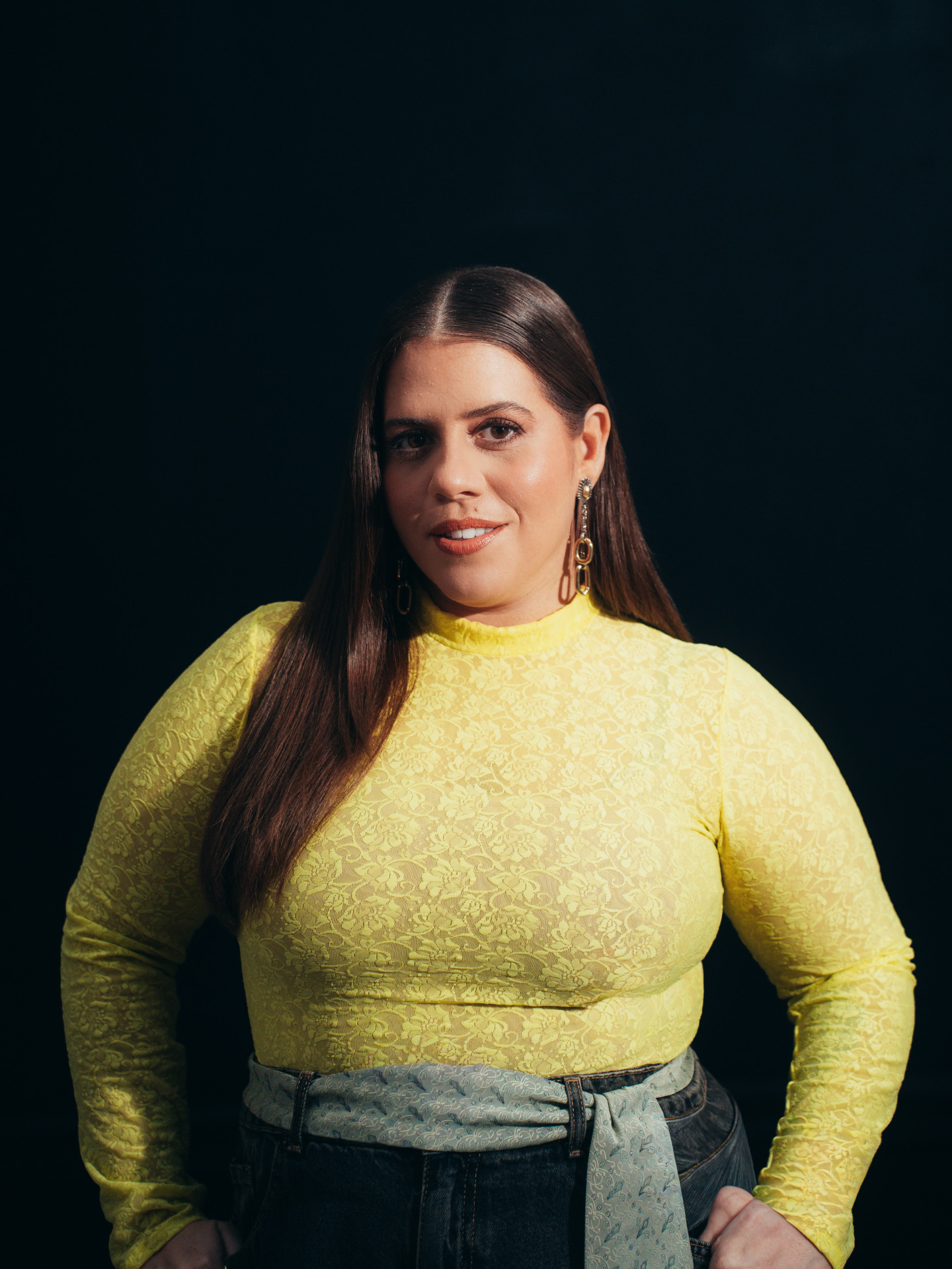 Grávida de oito meses, Tati Machado sorri ao lado de seu marido, segurando um cartão com o nome do bebê.