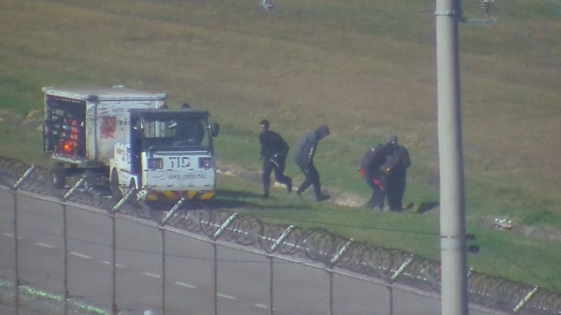 Imagem de uma multidão de migrantes em Ceuta, Espanha, com uma barreira de segurança ao fundo.