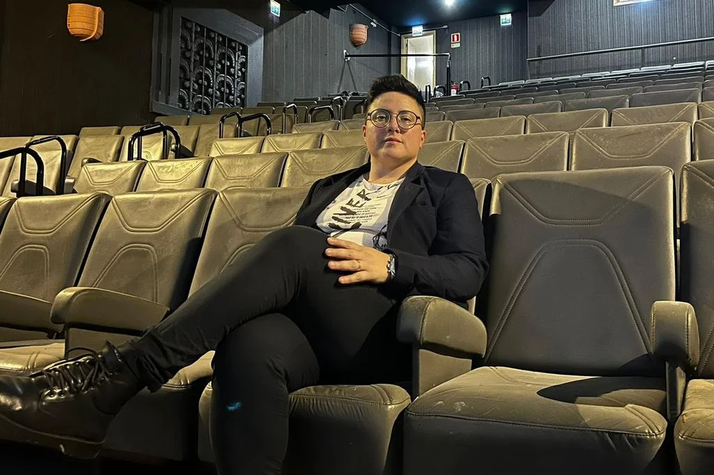 Família sorridente em frente a uma tela de cinema com cartazes de filmes ao fundo.